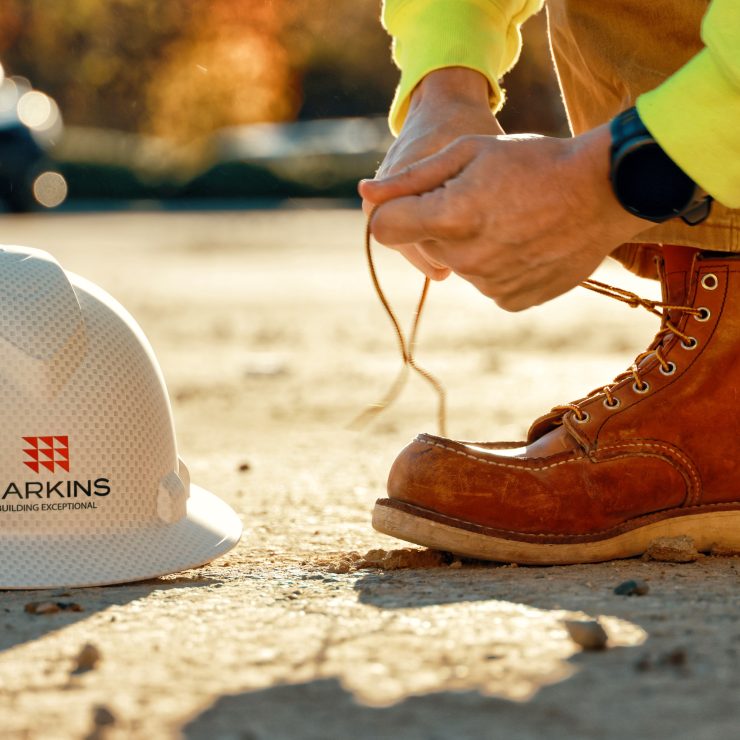 Harkins employee tying up work boots with helmet in frame.